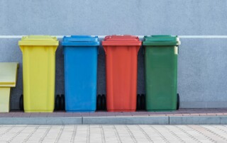 four assorted-color trash bins beside gray wall